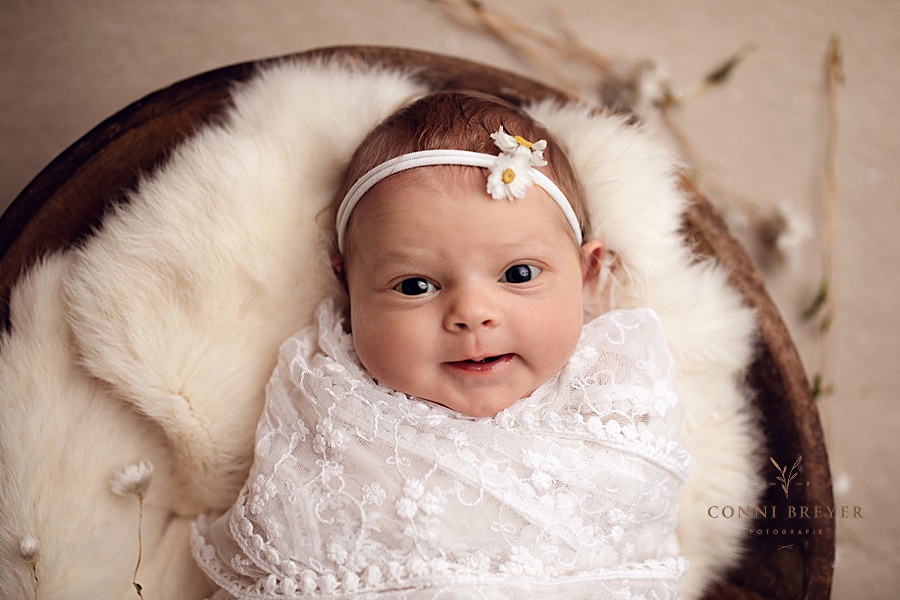 Süßes Baby mit offenen Augen und lächelnd in creme mit Gänseblümchen bei conni breyer Fotografie nähe Wangen